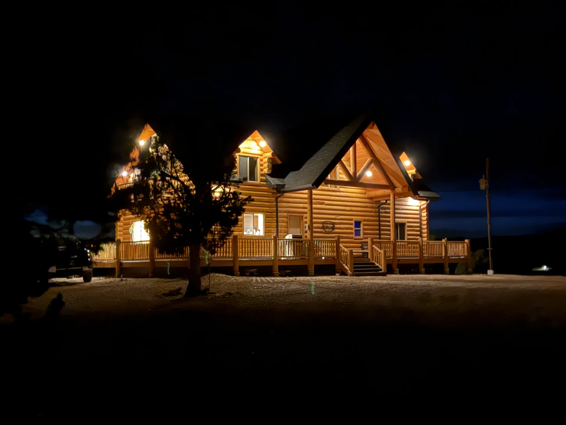 A finished log cabin lit up at night, warm light glowing from its windows and gable peaks against a dark sky